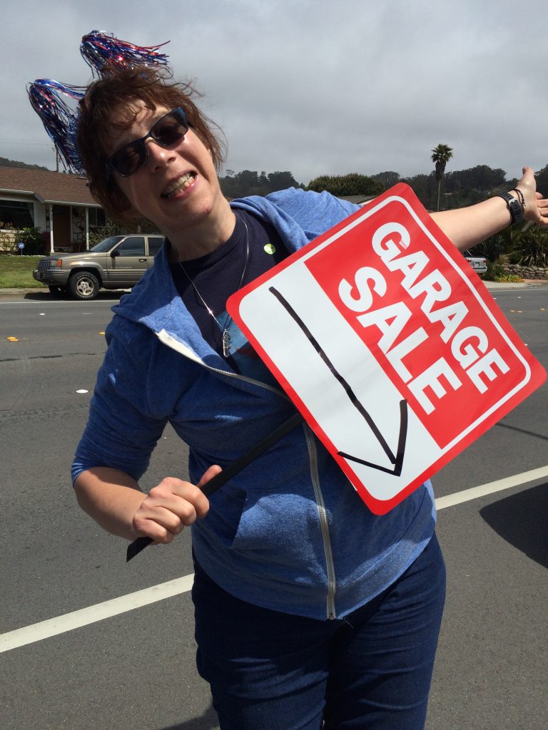 Cheryl smiling and waving a garage sale sign